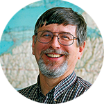 headshot of older white male with salt and pepper hair smiling at camera in front of a map
